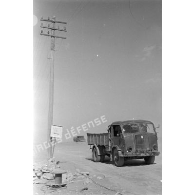 Passage de camions le long de poteaux télégraphiques et à coté d'un panneau indiquant un point de rassemblement.