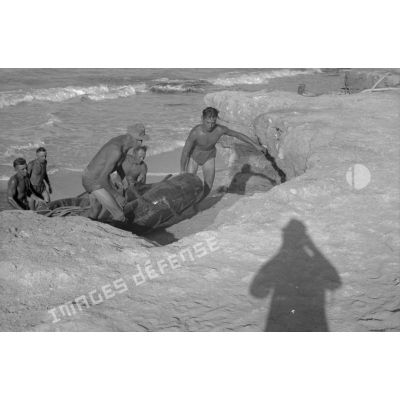 Après avoir déposé un tuyau pour pomper l'eau de mer, des soldats tirent un canot pneumatique sur la plage.