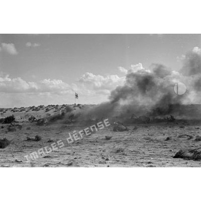 Des débris d'un avion en feu près d'un drapeau de la croix rouge dans le désert.
