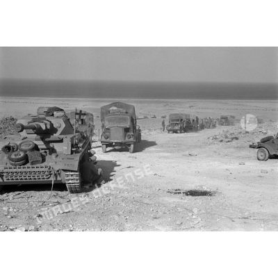 Un char Panzer IV (Pz-IV Ausf-F2) est immobilisé le long de la route tandis qu'un convoi roule vers la passe d'Halfaya.