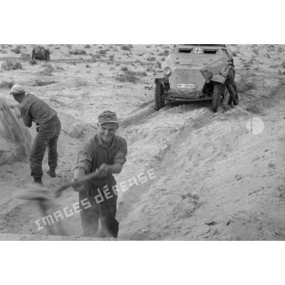 Des soldats créent un passage à la pelle dans le sable pour un blindé Sd.Kfz.251 Ausf-C.