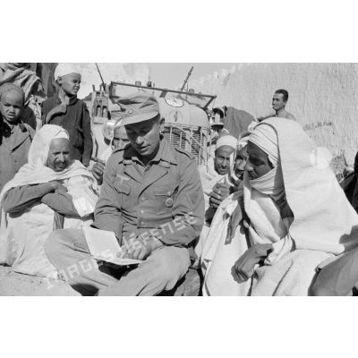 Un Leutnant et un Gefreiter distribuent des portraits de Rommel et discutent avec les habitants du village.