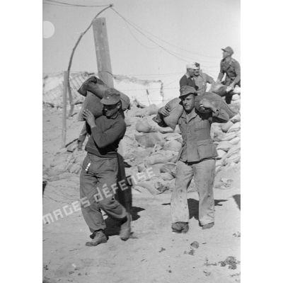 Deux soldats transportent des sacs de sable.