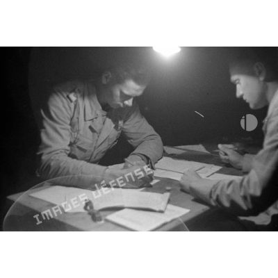 Un Oberleutnant et un soldat établissent des rapports ou des tables de tir éclairés par une lampe nue.