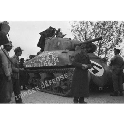 Des soldats allemands entourent un char américain M4A1 recouvert d'un drapeau et d'une inscription.