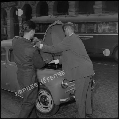 Un lieutenant déposant ses bagages dans le coffre d'une voiture Citroën 4CV.