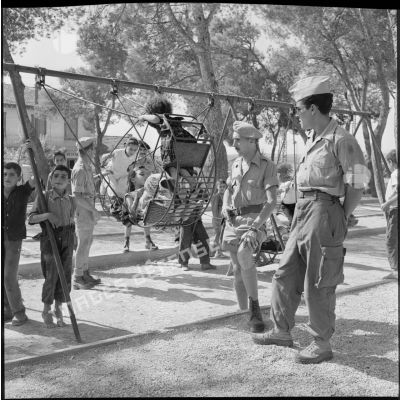 Des soldats du 18e régiment de chasseurs parachutistes(RCP) regardant des enfants s'amuser sur des balançoires.