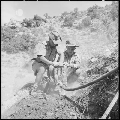 Deux soldats du 105e RG dont un jeune rappelé percent le roc à l'aide d'un marteau-piqueur.