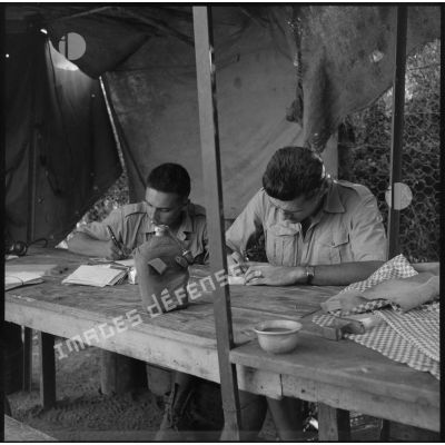 Assis à une table, deux soldats du 28e BCA rédigent leur courrier.