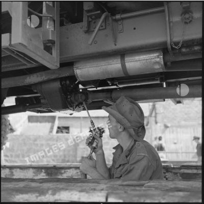 Un soldat de la 69e CRD installé dans une fosse lubrifie un arbre de transmission situé sous le camion.