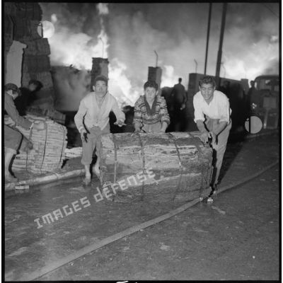 Plusieurs ouvriers éloignent des palettes de liège de l'incendie.