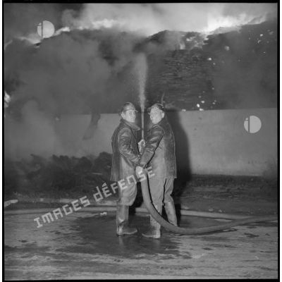 Deux pompiers tentent de contenir les flammes.