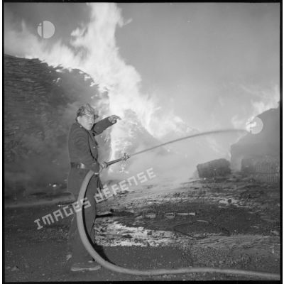 Un pompier arrose les flammes avec sa lance à incendie.