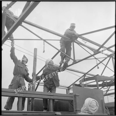 Deux soldats et un jeune algérien travaillant sur le toit d'un hangar en chantier.