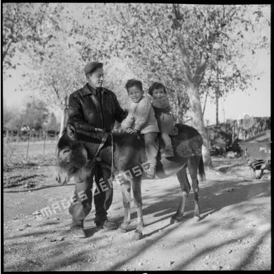 Deux jeunes enfants algériens à dos de mulet posent avec un soldat à Blida.