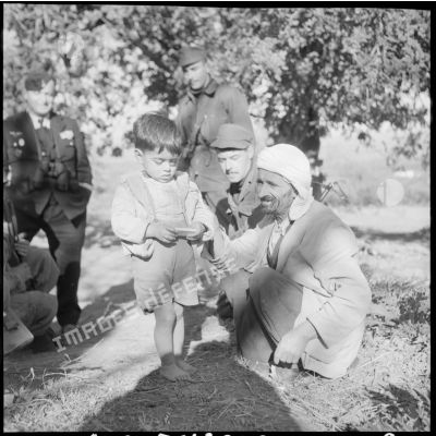 Un jeune enfant algérien tient un gâteau donné par des soldats.