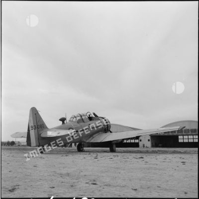 Un avion North American T6 devant des hangars.
