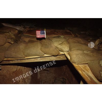 Entrée surmontée d'un drapeau d'un abri américain, enterré et protégé par des sacs de sable, en ZDO (zone de déploiement opérationnel) Olive lors d'une alerte de nuit.