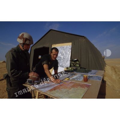 Vie quotidienne en ZDO (zone de déploiement opérationnel) Olive : un officier et un colonel étudient des cartes de la région étalées sur une table devant une tente au PC (poste de commandement).