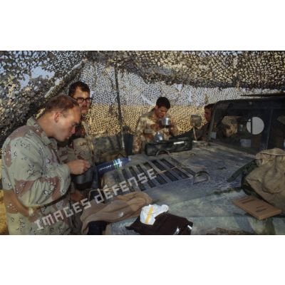 Pause café sur le capot d'un véhicule Hummer américain sous un filet de camouflage sur un poste en ZDO (zone de déploiement opérationnel) Olive.