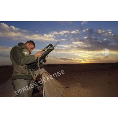 En ZDO (zone de déploiement opérationnel) Olive, sentinelle armée d'un fusil d'assaut FAMAS devant sa tente au coucher de soleil.
