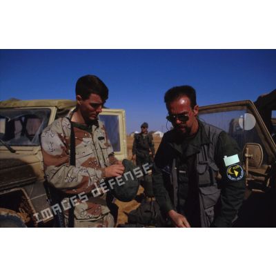 En ZDO (zone de déploiement opérationnel) Olive, un caméraman de l'ECPA (Etablissement cinématographique et photographique des Armées) devant un véhicule Peugeot P4 en compagnie d'un soldat américain.