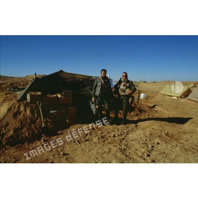 En ZDO (zone de déploiement opérationnel) Olive, le caméraman et le preneur de son de l'ECPA (Etablissement cinématographique et photographique des Armées) posent devant leur tente-abri. Des cartons font office de sacs à terre.