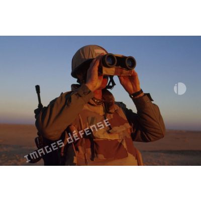 En ZDO (zone de déploiement opérationnel) Olive, un soldat est posté en observation dans le désert, équipé de jumelles.