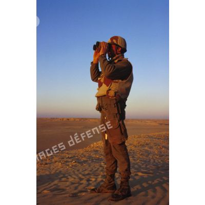 En ZDO (zone de déploiement opérationnel) Olive, un soldat est posté en observation dans le désert, équipé de jumelles.