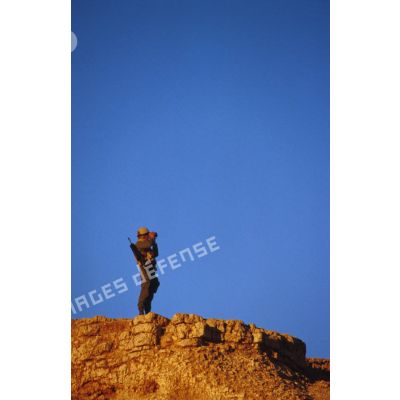 En ZDO (zone de déploiement opérationnel) Olive, un soldat équipé de jumelles est posté en observation au sommet d'une butte.