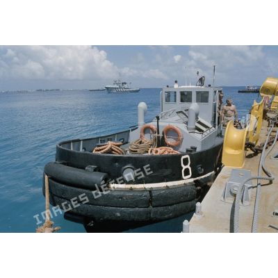 La barge de mise en place des containers est déplacée par les remorqueurs de la Marine dans le port de Mururoa. [Description en cours]