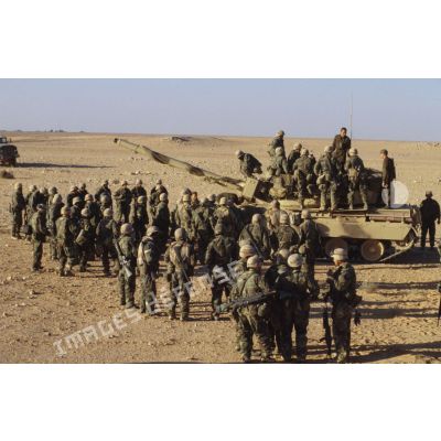 En ZDO (zone de déploiement opérationnel) Olive, un groupe de sodats américains entourent ou sont juchés sur un char lourd de combat AMX-30 B2.