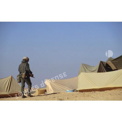En ZDO (zone de déploiement opérationnel) Olive, un soldat armé d'un fusil d'assaut FAMAS déambule dans un campement.