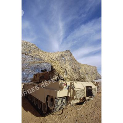 En ZDO (zone de déploiement opérationnel) Olive, un char de combat Abrams-M1 américain entre sous un filet de camouflage tendu dans le désert.