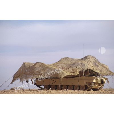En ZDO (zone de déploiement opérationnel) Olive, un char de combat Abrams-M1 américain est installé sous un filet de camouflage tendu dans le désert.