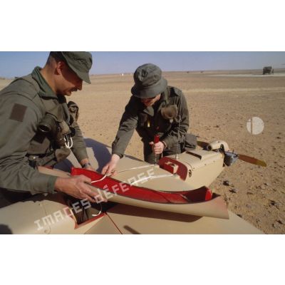 Mise en oeuvre du système de drones MART Mk II en ZDO (zone de déploiement opérationnel) Olive par deux soldats qui s'affairent autour de l'ALT (avion léger télécommandé) à voilure fixe.