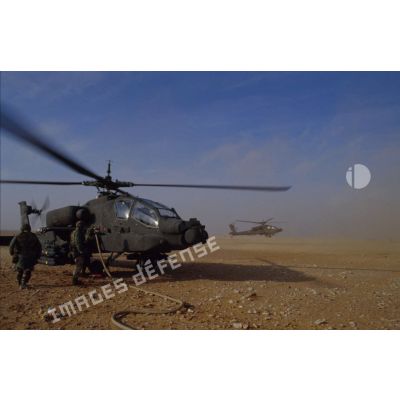 En ZDO (zone de déploiement opérationnel) Olive, des soldats ravitaillent en carburant un hélicoptère de combat américain Hughes-AH 64 Apache de retour de mission, rotors tournant.