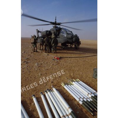 En ZDO (zone de déploiement opérationnel) Olive, des soldats ravitaillent en carburant et approvisionnent  en munitions un hélicoptère de combat américain Hughes-AH 64 Apache de retour de mission, rotors tournant.