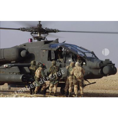En ZDO (zone de déploiement opérationnel) Olive, des soldats approvisionnent en munitions et ravitaillent en carburant un hélicoptère de combat américain Hughes-AH 64 Apache rotors tournant dans le désert.