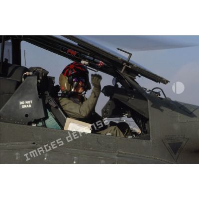 En ZDO (zone de déploiement opérationnel) Olive, portrait d'un copilote-tireur d'hélicoptère de combat américain Hughes-AH 64 Apache au cockpit, verrière latérale relevée.