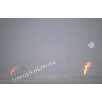 Puits de pétrole en feu derrière un pylone électrique.