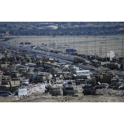 Un convoi de véhicules alliés emprunte la route au milieu d'un cimetière d'épavse de camions et de blindés irakiens détruits ou abandonnés à la sortie de Koweit City.