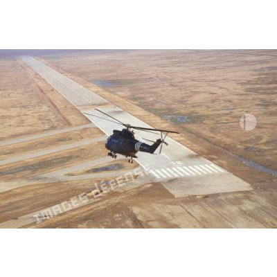 Vue aérienne d'un hélicoptère de transport Puma SA-330 de l'ALAT (aviation légère de l'armée de terre) survolant la piste d'envol de la base aérienne d'Al Salman, endommagée par les soins du 6e REG (régiment étranger du génie).