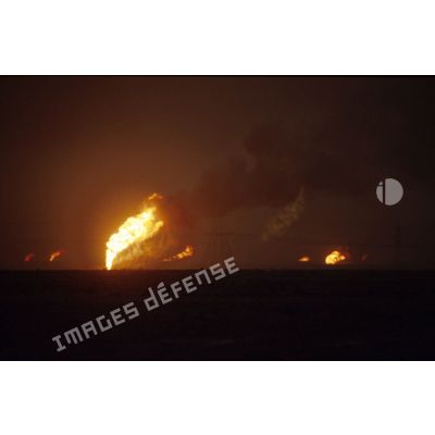 Puits de pétrole en feu aux environs de Koweit city derrière un pylone électrique.