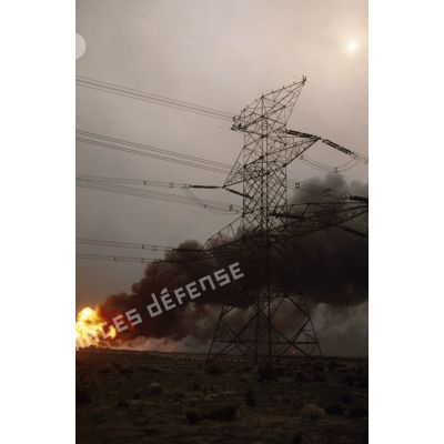 Puits de pétrole en feu aux environs de Koweit city derrière un pylone électrique.