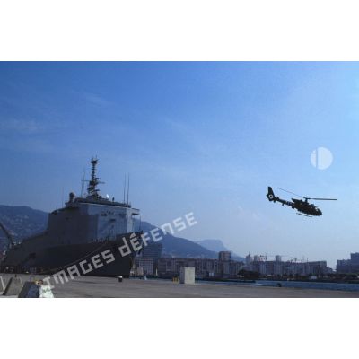Un hélicoptère de combat Gazelle du 3e RHC (régiment d'hélicoptères de combat) décolle d'un quai du port de Toulon. En arrière-plan le TCD (transport de chalands de débarquement) Foudre est amarré au quai.