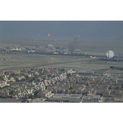Vue aérienne de la ville de Koweit City. A l'arrière-plan, des puits de pétrole brûlent.