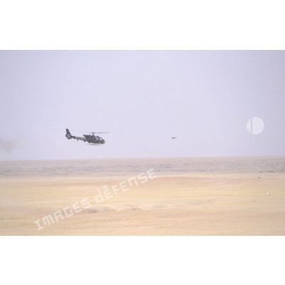 Hélicoptère de combat Gazelle SA-342 en vol d'entraînement au tir de missiles HOT. Le missile est en vol devant l'hélicoptère.