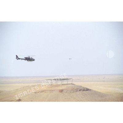 Hélicoptère de combat Gazelle SA-342 en vol d'entraînement au tir de missiles HOT. Le missile est en vol devant l'hélicoptère.