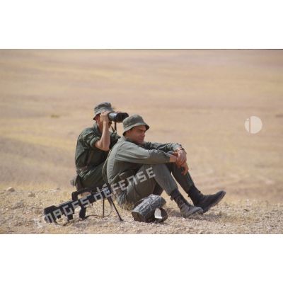 Soldats scrutant le désert à l'aide de jumelles, assis à côté d'un fusil d'assaut FAMAS.